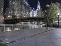 a paved sidewalk next to the water and some buildings at night in a city area