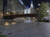 a paved sidewalk next to the water and some buildings at night in a city area