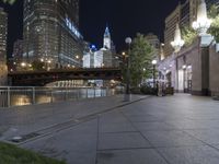 a paved sidewalk next to the water and some buildings at night in a city area