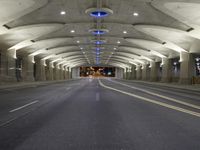 empty roadway with lights at night, with buildings in background in long tunnel in large city