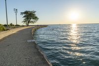 a concrete path leading over water near trees and grass near the ocean, with sun setting behind them