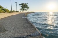 a concrete path leading over water near trees and grass near the ocean, with sun setting behind them