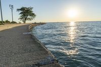 a concrete path leading over water near trees and grass near the ocean, with sun setting behind them