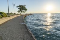 a concrete path leading over water near trees and grass near the ocean, with sun setting behind them