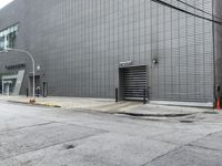 a white fire hydrant sitting next to a tall grey building on a sidewalk near an orange cone