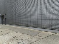 a man in suit walking down a street next to a silver building with latticed metal screen behind him