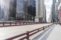 many tall buildings are behind the benches on a sidewalk near a bridge and walkway line