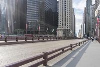 many tall buildings are behind the benches on a sidewalk near a bridge and walkway line