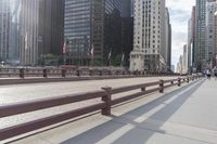 many tall buildings are behind the benches on a sidewalk near a bridge and walkway line