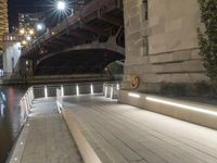 a white bench sitting on top of a sidewalk next to a bridge at night with lights above it