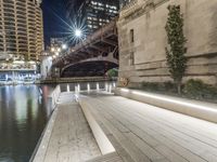 a white bench sitting on top of a sidewalk next to a bridge at night with lights above it