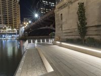 a white bench sitting on top of a sidewalk next to a bridge at night with lights above it