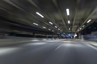 a long road running through an illuminated tunnel at night with cars passing by on it