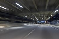 a long road running through an illuminated tunnel at night with cars passing by on it