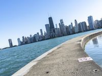 an empty sidewalk that leads to the city of chicago's skyline, which is in the middle of the lake