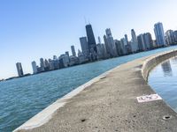 an empty sidewalk that leads to the city of chicago's skyline, which is in the middle of the lake