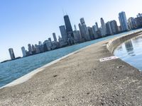 an empty sidewalk that leads to the city of chicago's skyline, which is in the middle of the lake