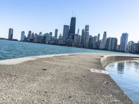 an empty sidewalk that leads to the city of chicago's skyline, which is in the middle of the lake