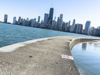 an empty sidewalk that leads to the city of chicago's skyline, which is in the middle of the lake