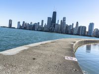 an empty sidewalk that leads to the city of chicago's skyline, which is in the middle of the lake