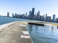 an empty sidewalk that leads to the city of chicago's skyline, which is in the middle of the lake