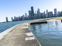 an empty sidewalk that leads to the city of chicago's skyline, which is in the middle of the lake