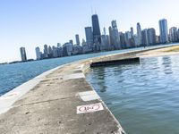 an empty sidewalk that leads to the city of chicago's skyline, which is in the middle of the lake