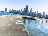 an empty sidewalk that leads to the city of chicago's skyline, which is in the middle of the lake