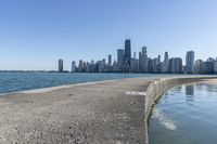 a concrete wall stretches down the side of the ocean towards a city skyline, on a sunny day