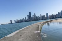 a concrete wall stretches down the side of the ocean towards a city skyline, on a sunny day