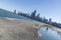 a concrete wall stretches down the side of the ocean towards a city skyline, on a sunny day