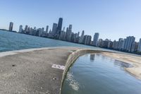 a concrete wall stretches down the side of the ocean towards a city skyline, on a sunny day