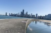 a concrete wall stretches down the side of the ocean towards a city skyline, on a sunny day