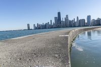 a concrete wall stretches down the side of the ocean towards a city skyline, on a sunny day