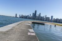 a concrete wall stretches down the side of the ocean towards a city skyline, on a sunny day