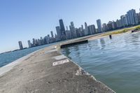 a concrete wall stretches down the side of the ocean towards a city skyline, on a sunny day