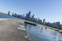 a concrete wall stretches down the side of the ocean towards a city skyline, on a sunny day