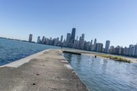 a concrete wall stretches down the side of the ocean towards a city skyline, on a sunny day