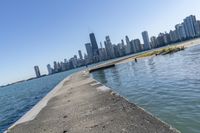 a concrete wall stretches down the side of the ocean towards a city skyline, on a sunny day