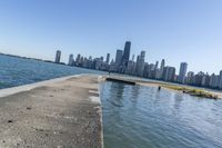 a concrete wall stretches down the side of the ocean towards a city skyline, on a sunny day