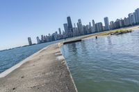 a concrete wall stretches down the side of the ocean towards a city skyline, on a sunny day