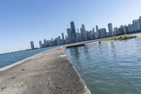 a concrete wall stretches down the side of the ocean towards a city skyline, on a sunny day