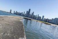 a concrete wall stretches down the side of the ocean towards a city skyline, on a sunny day