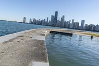 a concrete wall stretches down the side of the ocean towards a city skyline, on a sunny day