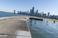 a concrete wall stretches down the side of the ocean towards a city skyline, on a sunny day