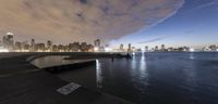 a city view at night with water in front and clouds above it with boats in the water