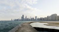 a concrete break wall overlooking the ocean with a city in the distance on the shore