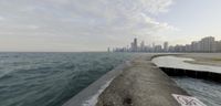 a concrete break wall overlooking the ocean with a city in the distance on the shore