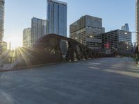 a person riding a skate board across a bridge in the sun light with buildings in the background