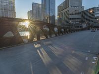 a person riding a skate board across a bridge in the sun light with buildings in the background